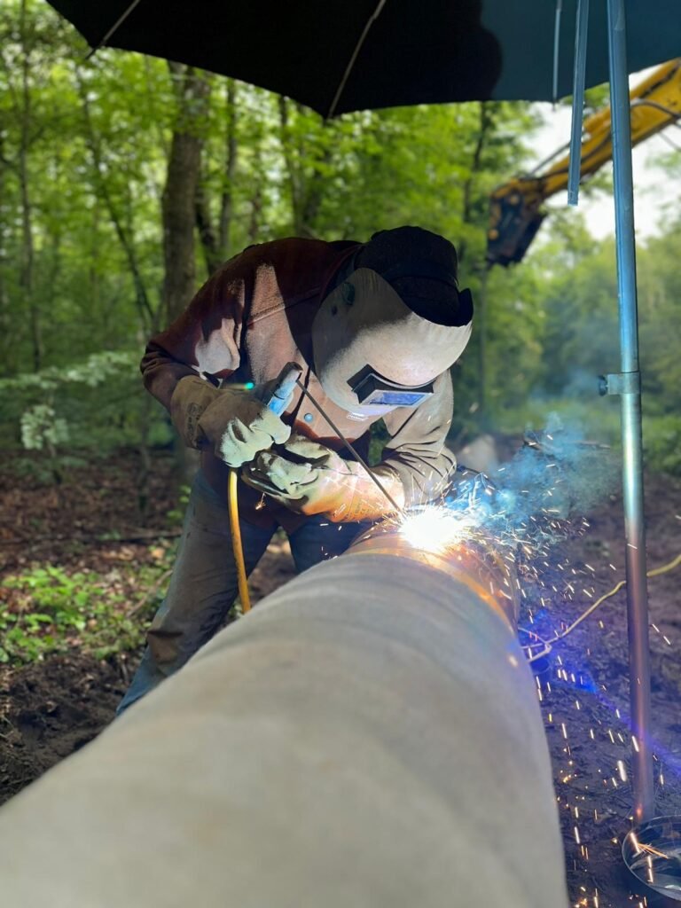 Schweißer schweißt eine Stahlrohrleitung unter einem Baustellenschirm