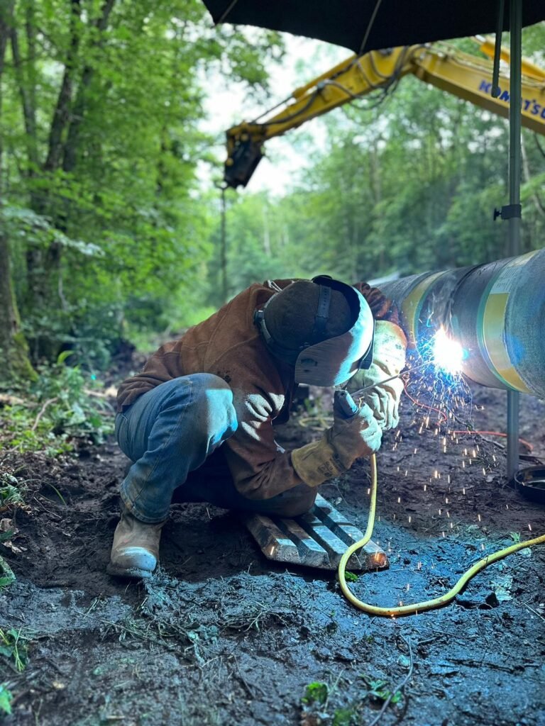 Schweißer kniet beim Schweißen einer Stahlrohrleitung im Wald